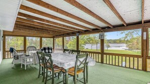 A covered outdoor dining area with a table and chairs, a wooden ceiling, and a view of the surrounding landscape.