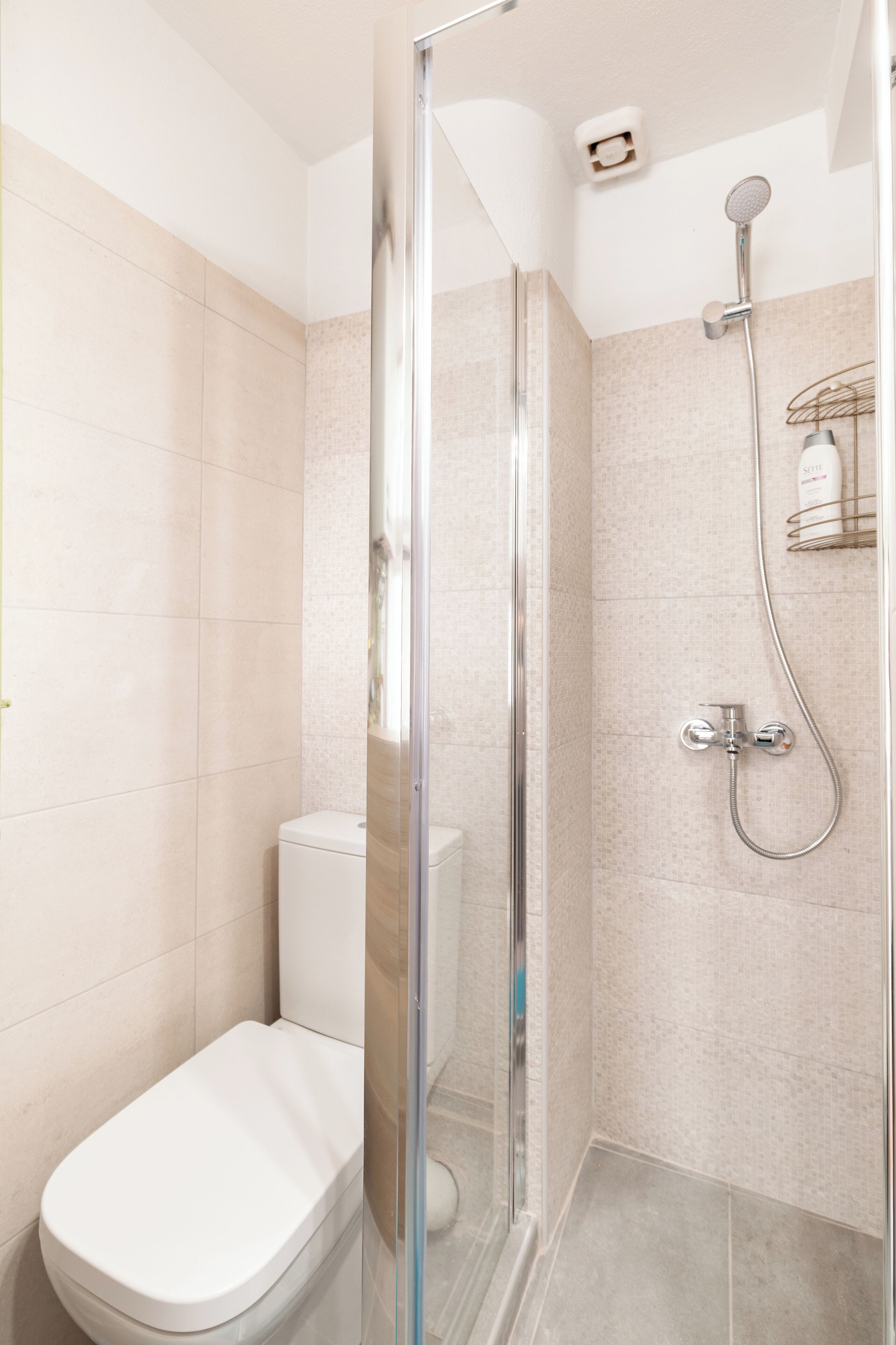 A modern bathroom with a glass-enclosed shower, a toilet, and a showerhead mounted on the wall.
