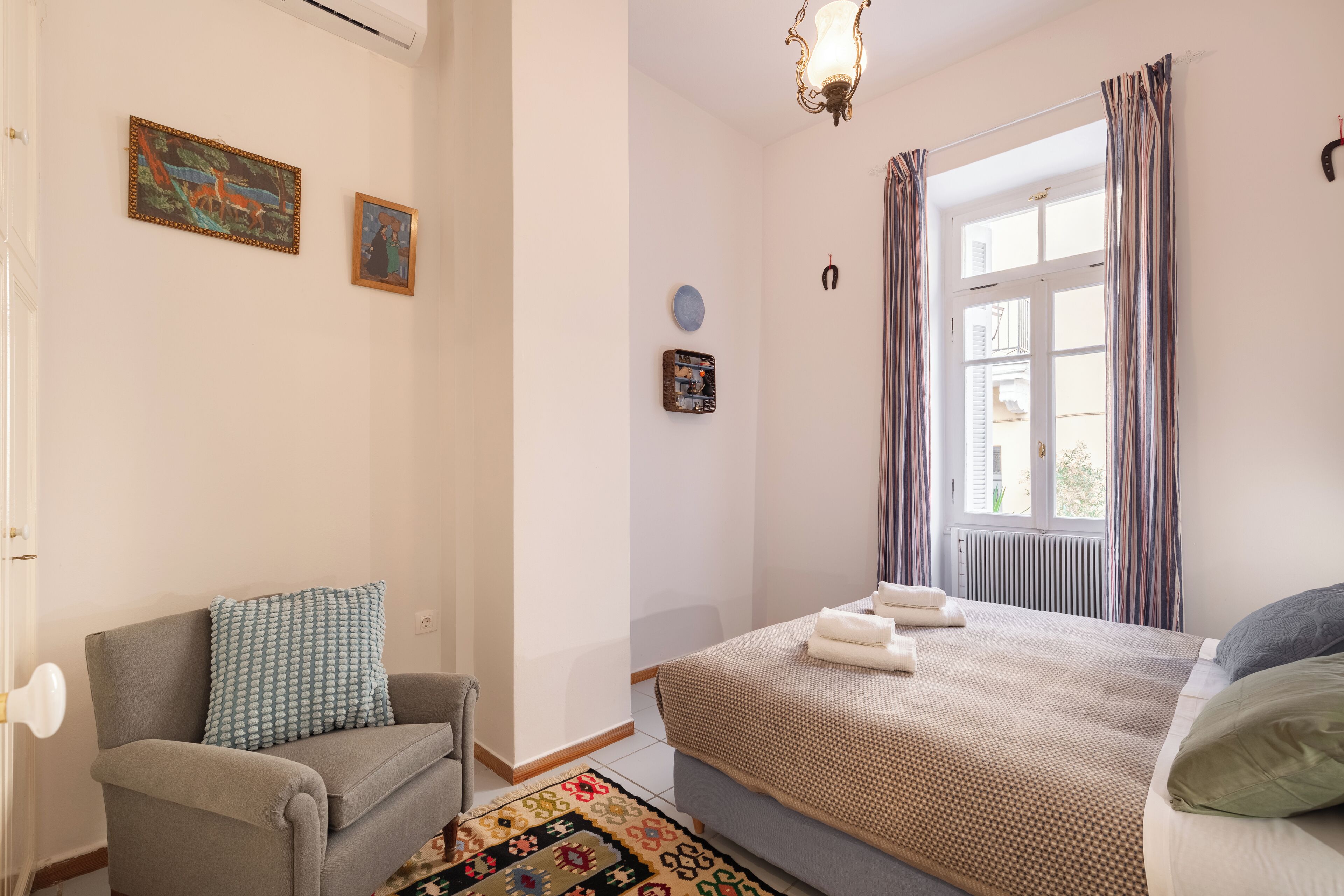 A bedroom with a bed, a chair, a window with curtains, and wall decorations.