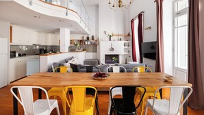 A modern kitchen with a wooden dining table and yellow chairs, a lofted living area with a staircase, and a large window with curtains. - Athenian Getaway Villa by Athenian Homes (Athens)
