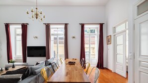 A modern living room with a wooden dining table, grey sofa, and yellow chairs. A flat-screen TV is mounted on the wall, and there are windows with curtains. - Athenian Getaway Villa by Athenian Homes (Athens)