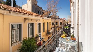 A narrow street with buildings on either side, a balcony with a table set for dining, and a clear blue sky. - Athenian Getaway Villa by Athenian Homes (Athens)
