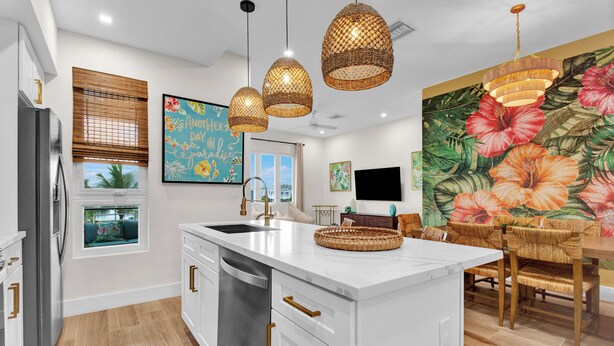 A modern kitchen with white cabinetry, a central island, and a dining area with wicker chairs.
