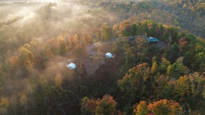 A forested area with a dome-shaped structure and a smaller building, surrounded by trees with autumn foliage.