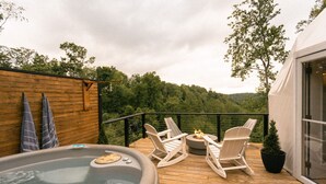 A wooden deck with a hot tub, two Adirondack chairs, and a potted plant.