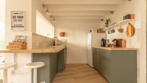 A kitchen with a central island, bar stools, a refrigerator, and a hanging light fixture.