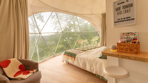 A cozy room with a large window, a bed, a chair, and a wall sign.