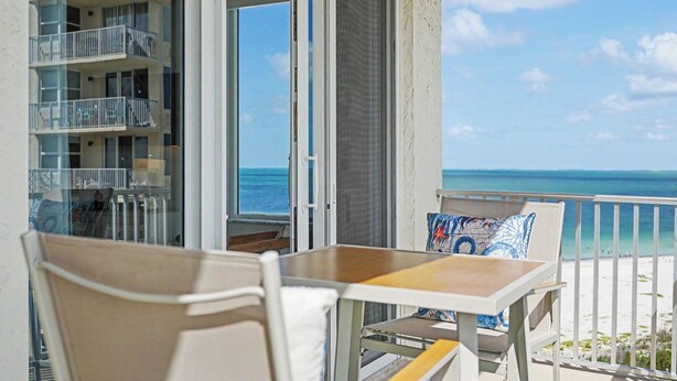 Ein Balkon mit Tisch und Stühlen mit Blick auf Strand und Meer.