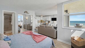 Ein Schlafzimmer mit Bett, Sofa, Fernseher und einem Fenster mit Meerblick.