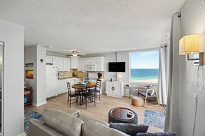 Une cuisine moderne avec des meubles blancs, un coin repas avec une table et des chaises, un téléviseur à écran plat fixé au mur et une vue sur la plage.