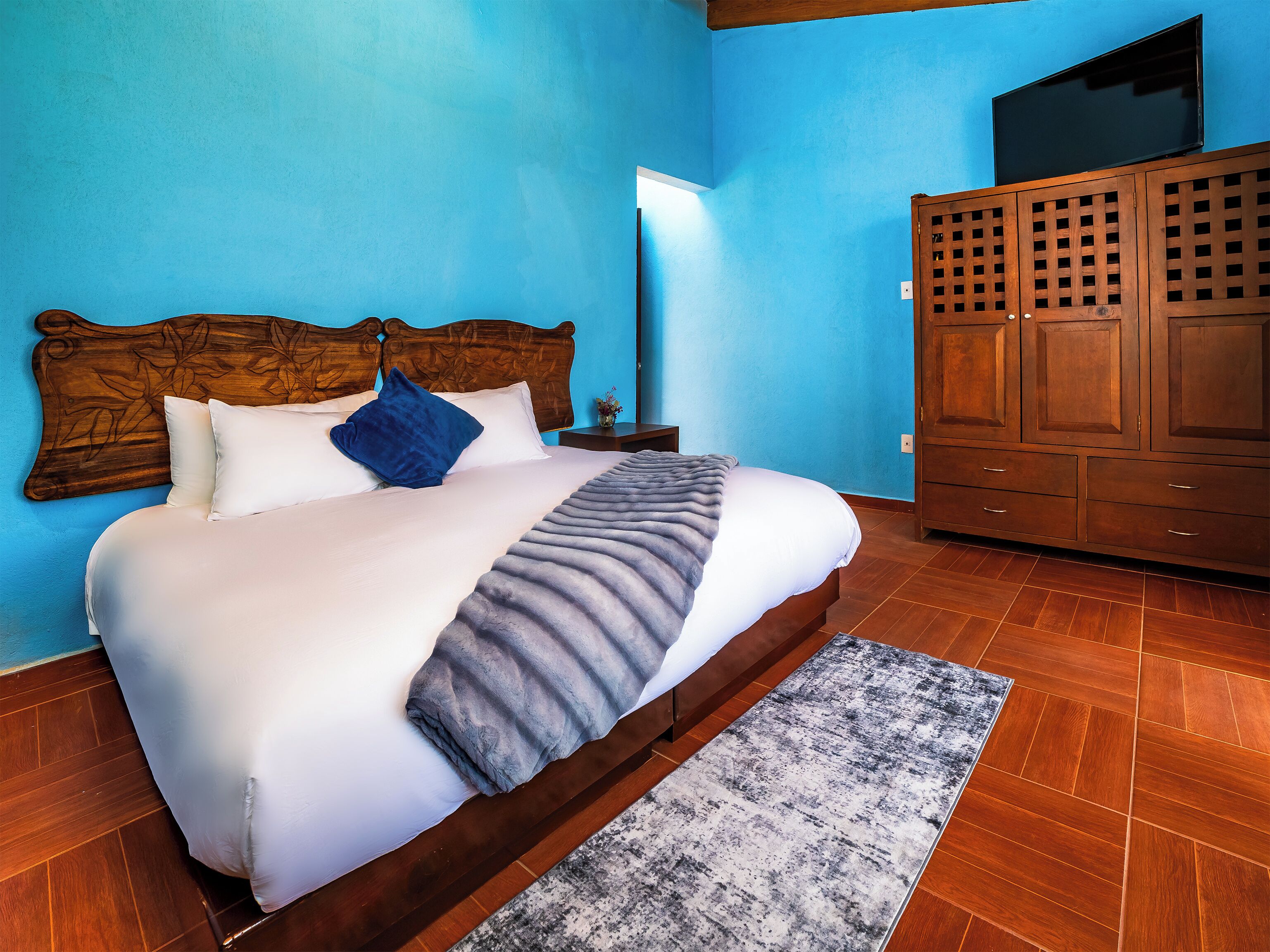 Una cama con cabecera de madera, pared azul y armario con diseño de celosía.