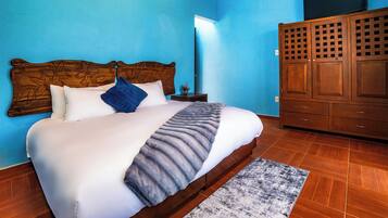Una cama con cabecera de madera, pared azul y armario con diseño de celosía.