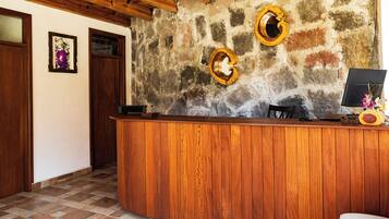 A reception desk with a wooden finish, a stone wall with two circular decorations, a computer monitor, and a vase with flowers.