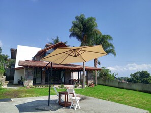 Una casa con un patio, mobiliario exterior y un paraguas grande.