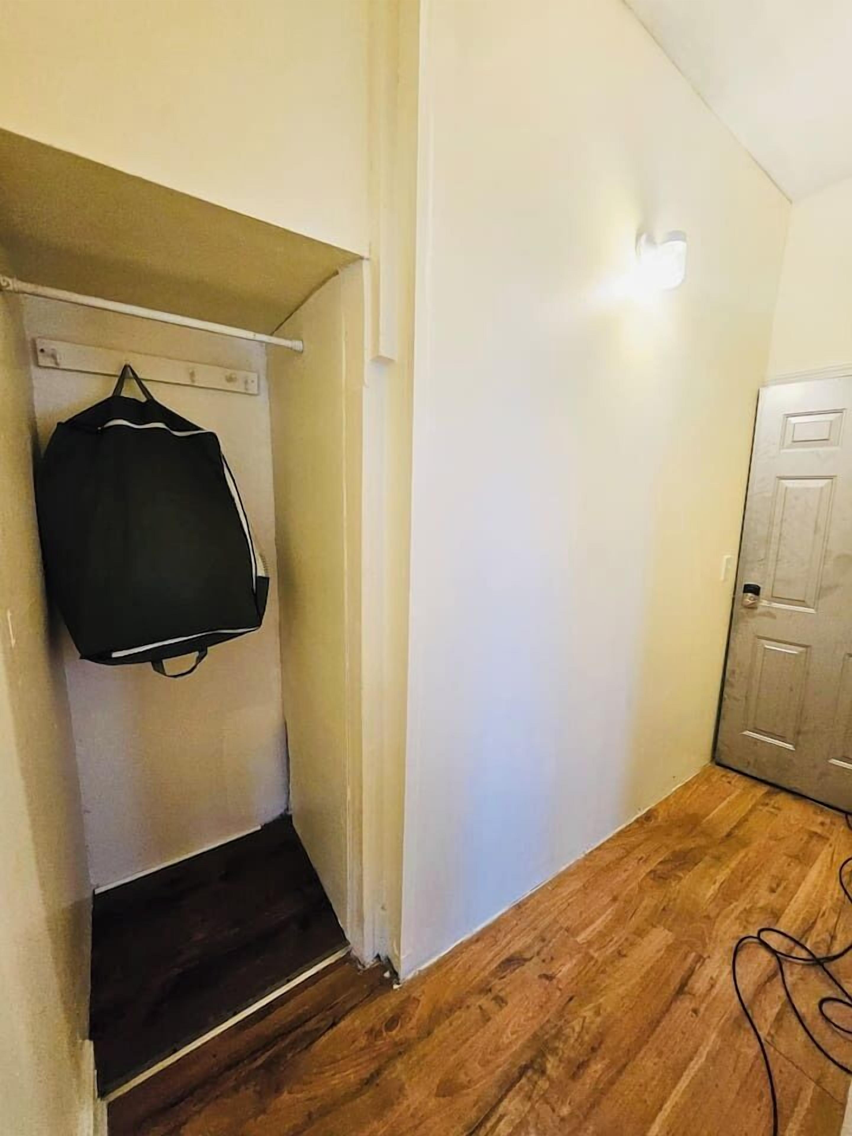 A hallway with a wooden floor, a door on the right, and a coat rack with a black jacket hanging on it.