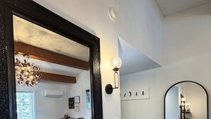 Ein Badezimmer mit einem großen Spiegel, einem weißen Waschbecken, einer Holzausstattung, einer Zimmerpflanze und einem sichtbaren Duschbereich.