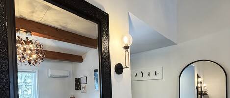 A bathroom with a large mirror, a white sink, a wooden vanity, a potted plant, and a visible shower area.