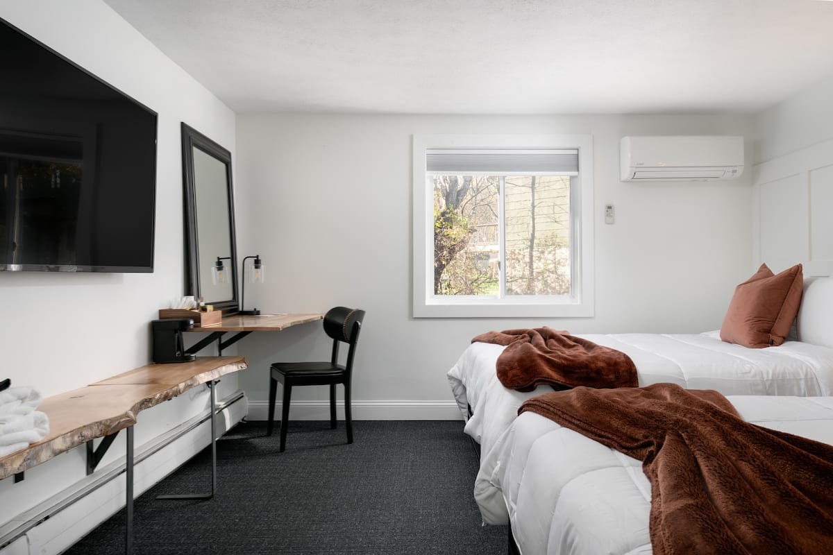Ein Schlafzimmer mit einem Bett, einem Schreibtisch, einem Stuhl, einem Fenster und einer Klimaanlage.