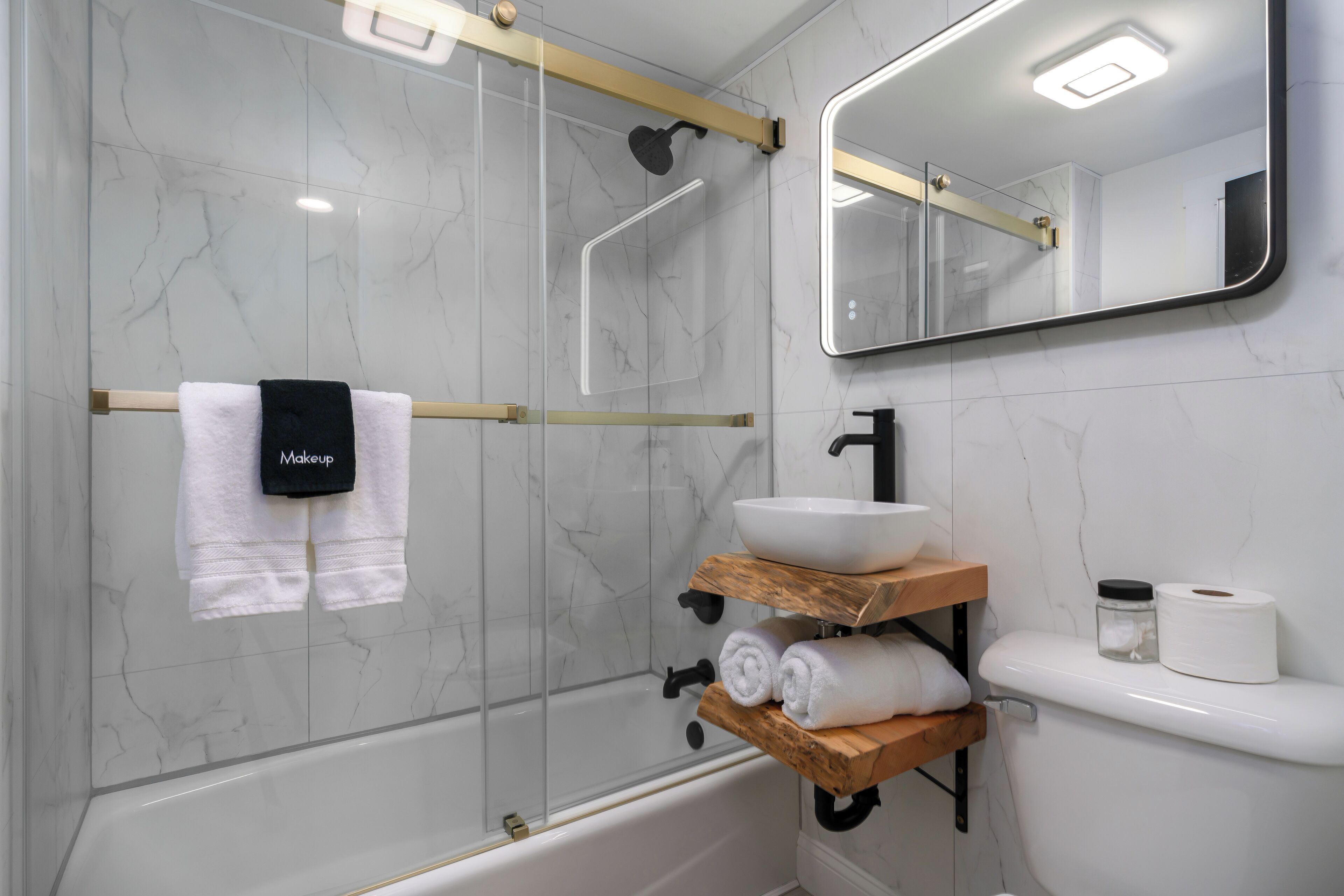 Un bagno moderno con doccia vetrata, vasca da bagno bianca, ripiano in legno con asciugamani, lavandino e WC.