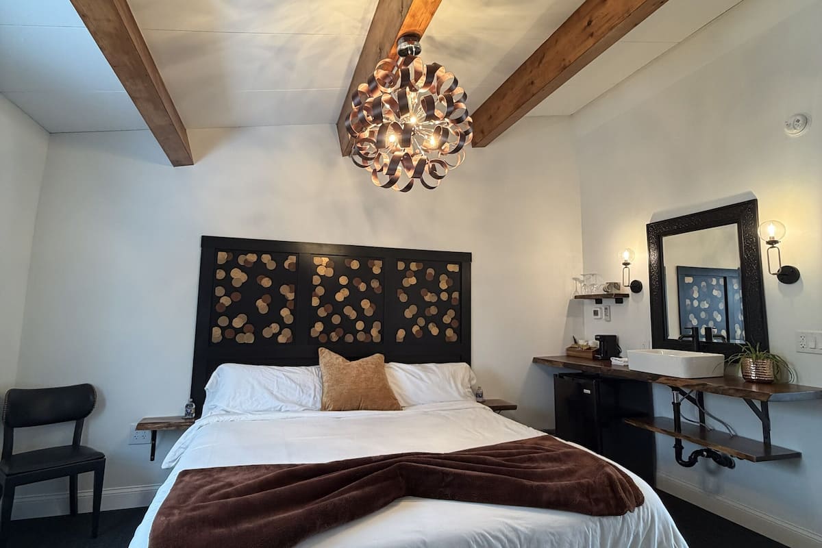Ein Schlafzimmer mit Bett, Holzboden, Wandverkleidung als Kopfteil, Nachttisch, Spiegel und einer Pendelleuchte.