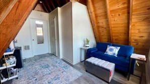 Ein gemütliches Dachzimmer mit einem blauen Sofa, einem kleinen Beistelltisch und einer Holzbalkendecke.
