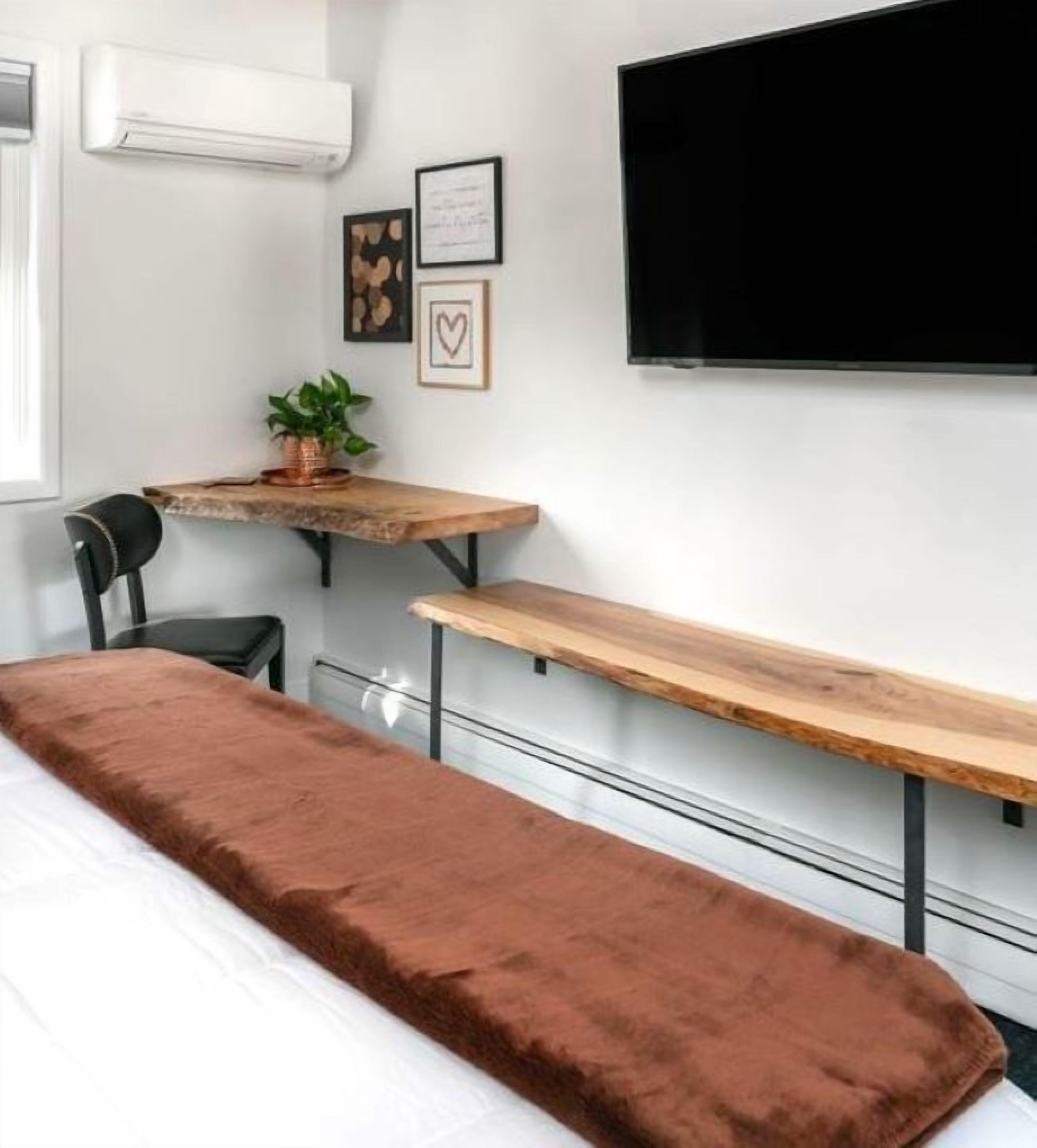 Un dormitorio con cama, escritorio, silla, televisor y planta en maceta.