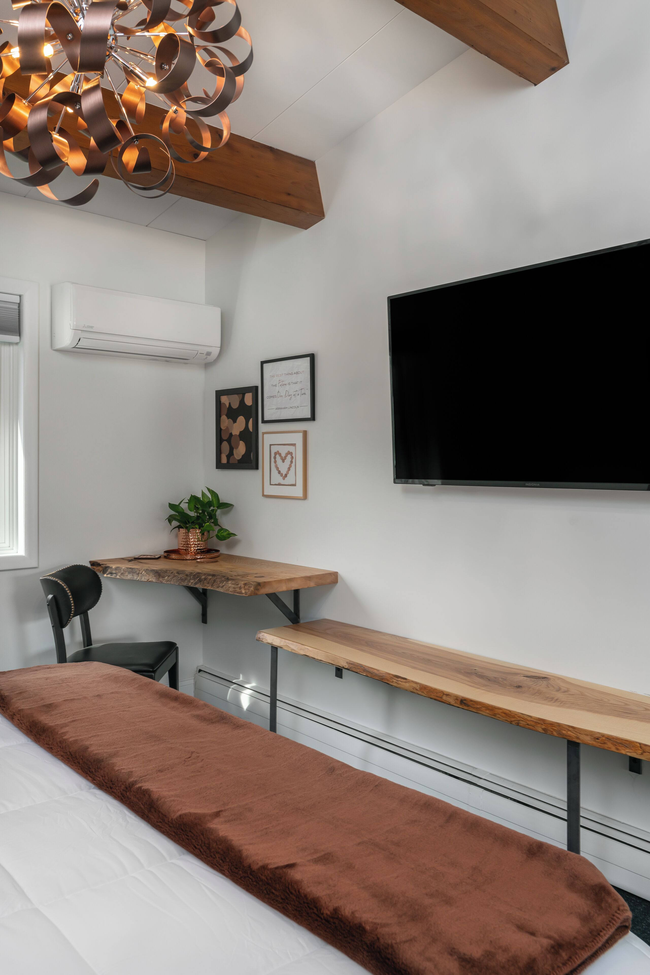 A modern bedroom with a large bed, a wooden bench, a TV, and a ceiling light fixture.