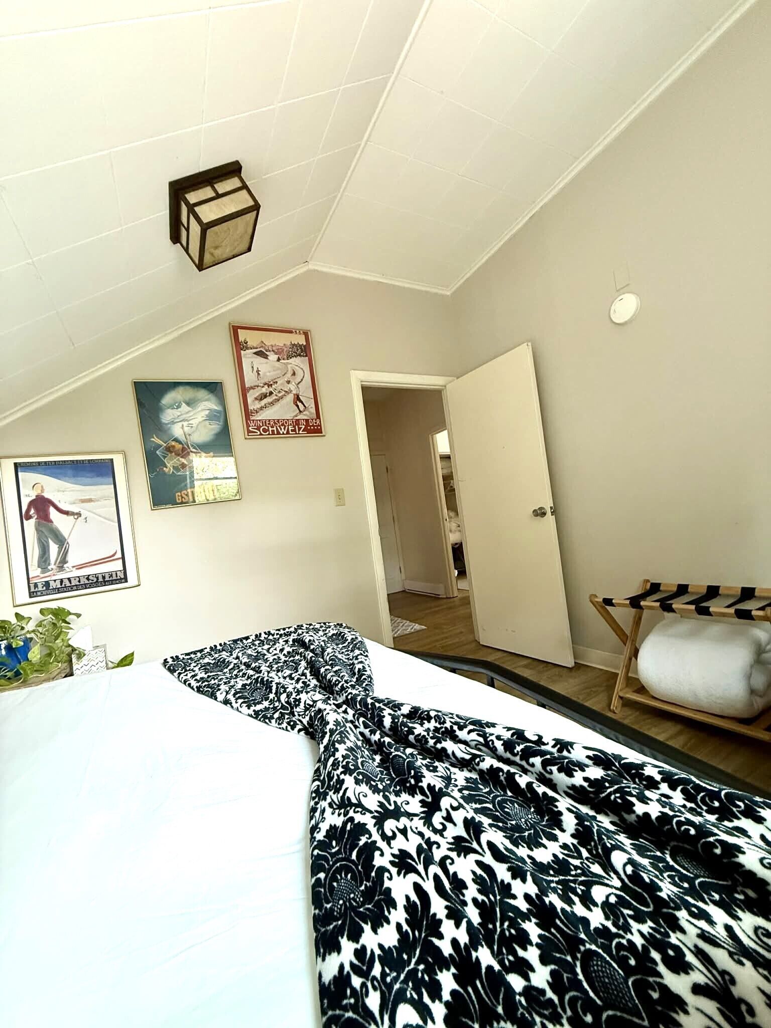A bedroom with a bed, a hanging light fixture, a door, and a wall-mounted shelf.