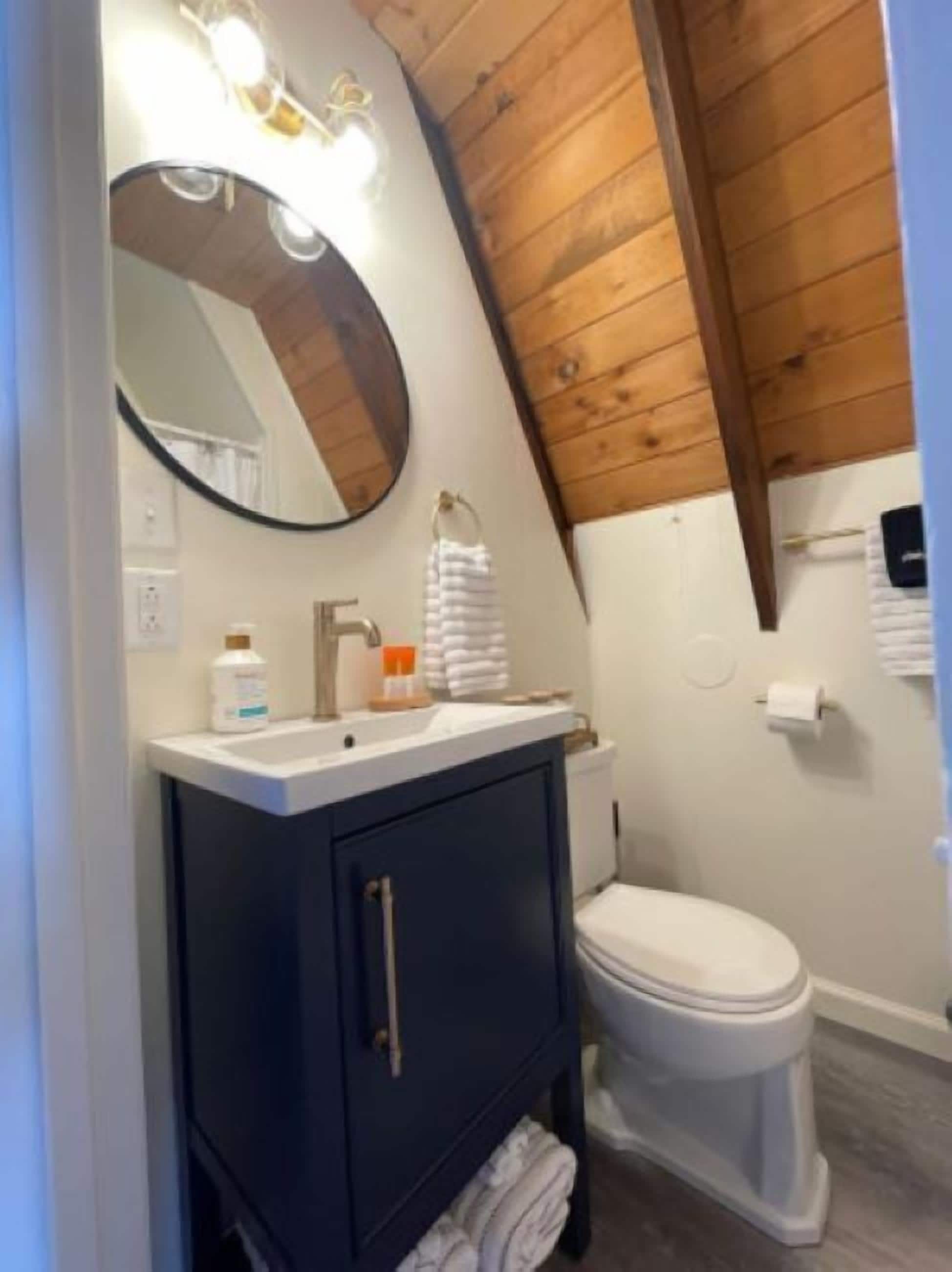A bathroom with a wooden ceiling, a white toilet, a dark blue cabinet, and a mirror with lights.