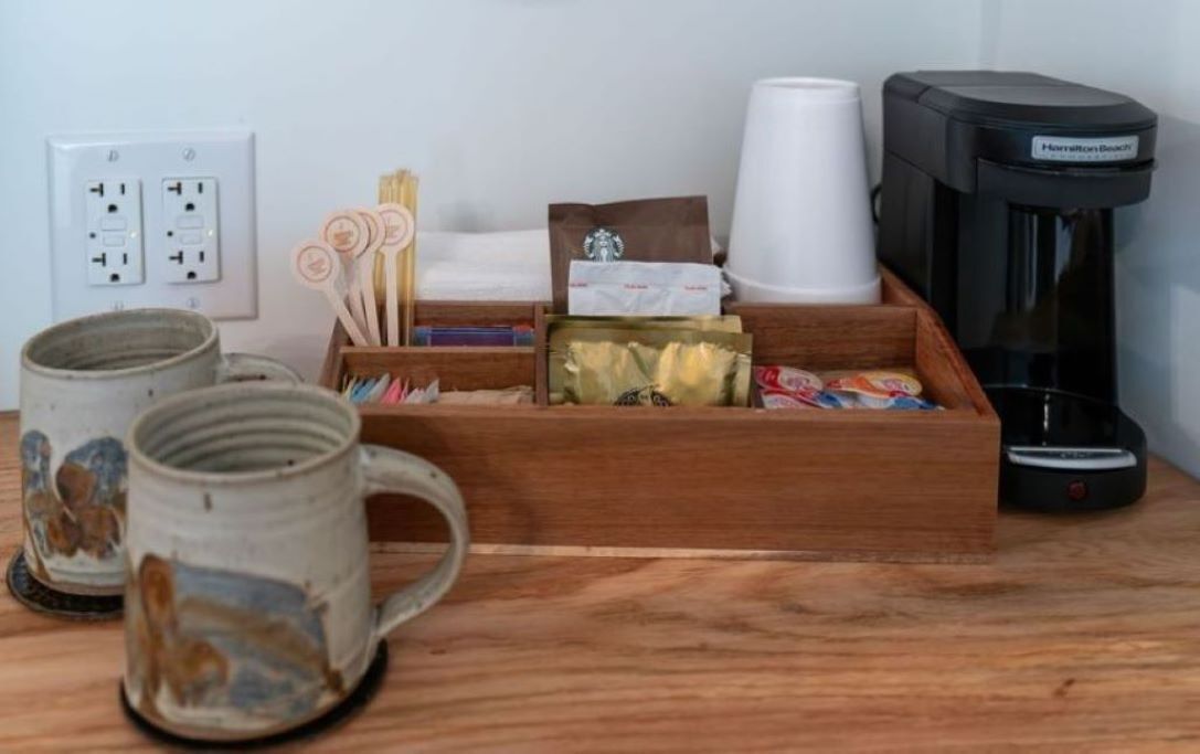 Een houten dienblad met koffiekopjes, een koffieapparaat en verschillende koffiekapsules.