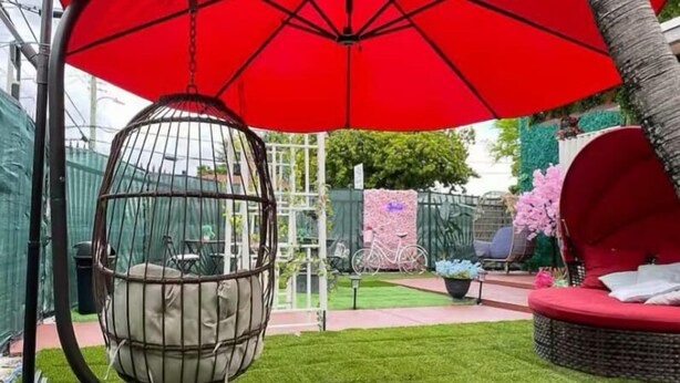A hanging chair under a red umbrella, a red swing set, and a red cushioned seating area in a garden setting. - Art Gardens Wynwood (Miami)