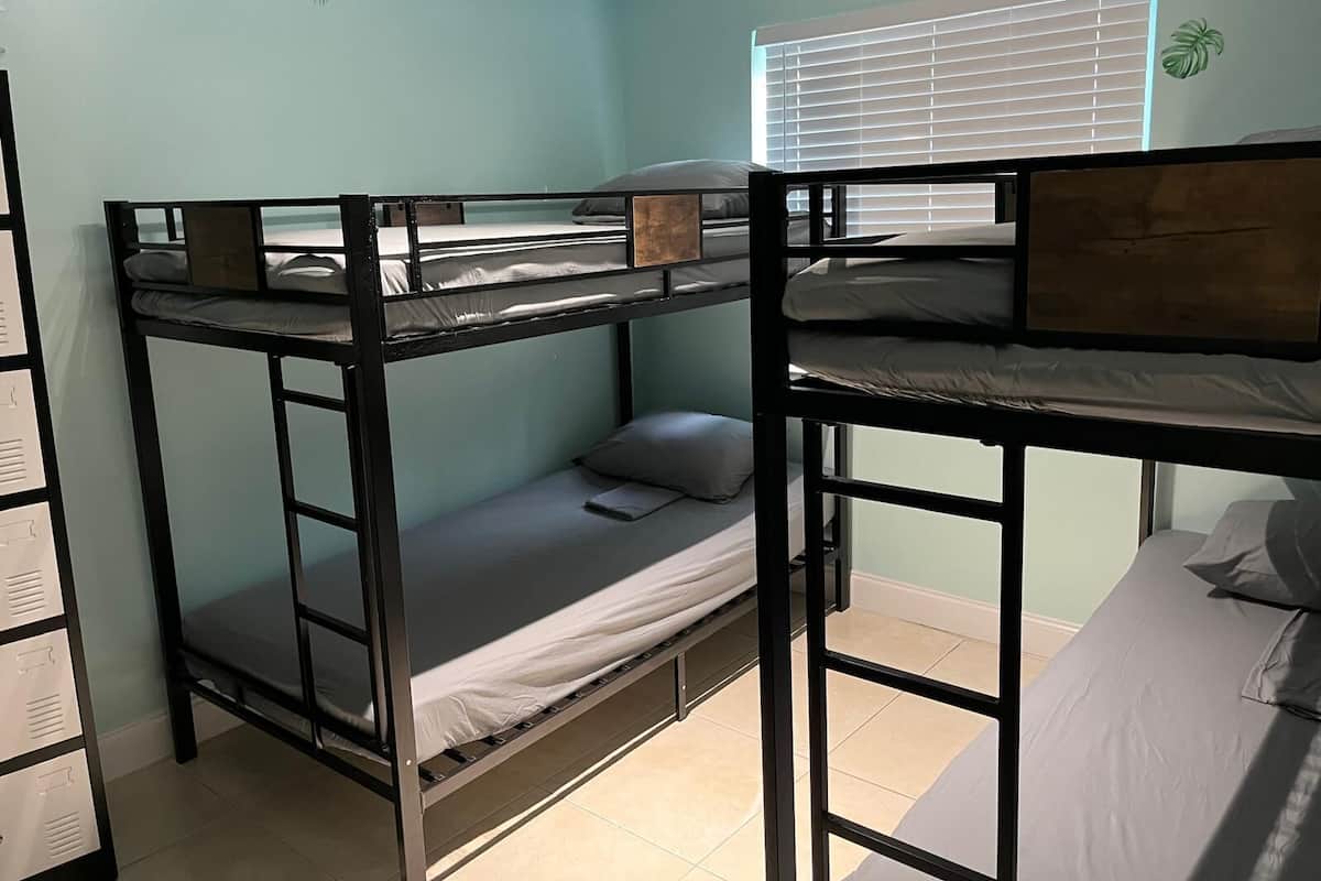 Dormitorio con literas, ventana, una planta y pared con diseño tropical.