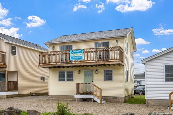 A two-story building with a balcony, a green door, and a sign indicating it is a rental property. - Attractive, updated 2-bedroom home, 5 min walk to beach, pets ok, onsite parking (Hampton)