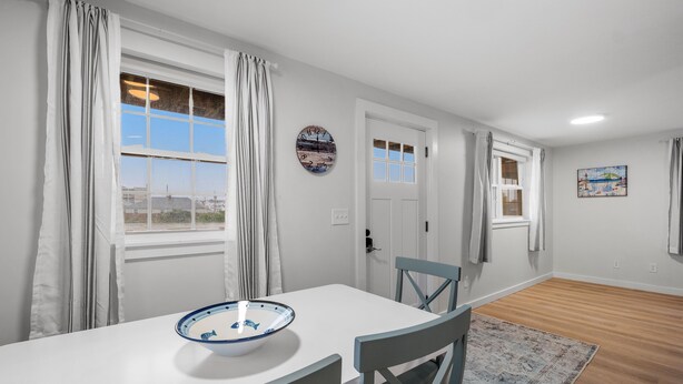 A dining area with a white table, blue and white bowl, two blue chairs, a patterned rug, and a view through a window. - Attractive, updated 2-bedroom home, 5 min walk to beach, pets ok, onsite parking (Hampton)