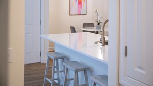 Una cocina moderna con una isla blanca, taburetes de bar y un comedor con sillas.