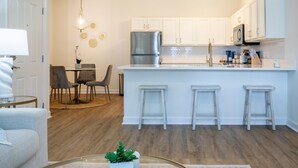 Una cocina moderna con gabinetes blancos, un refrigerador de acero inoxidable y una isla central con taburetes de bar.