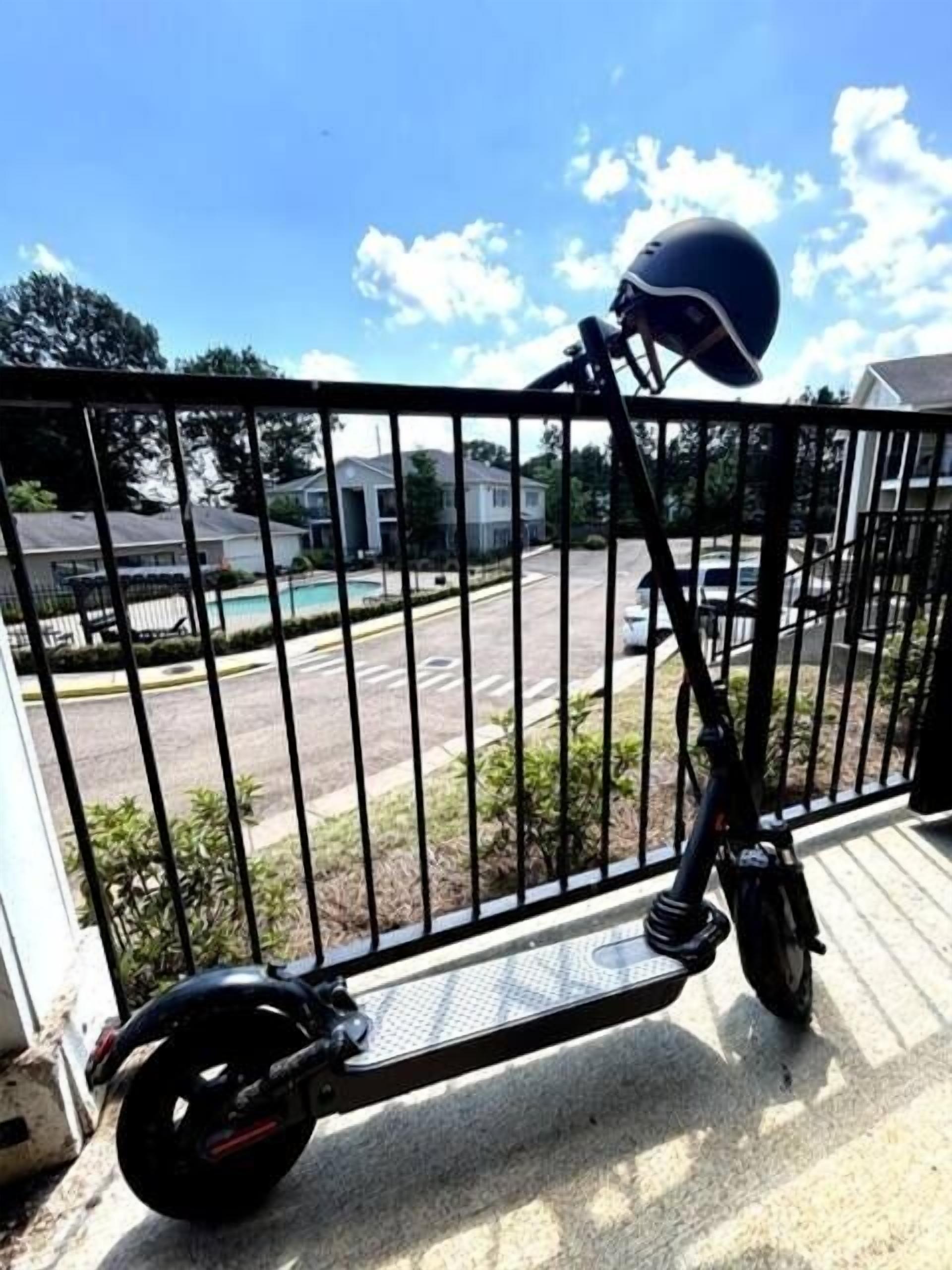 A stationary electric scooter parked near a metal fence with a view of a residential street and houses in the background.