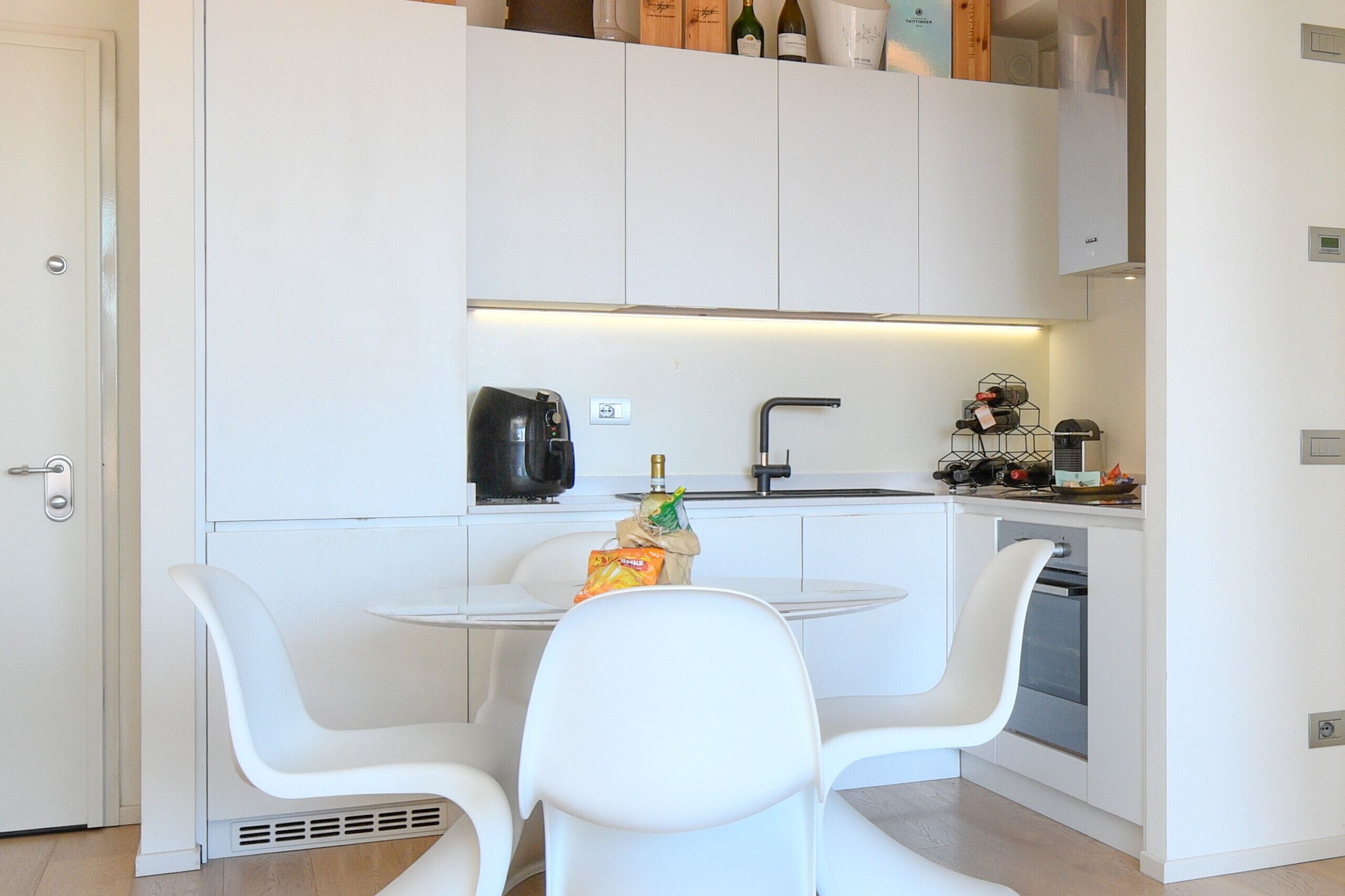 A modern kitchen with white cabinetry, a round dining table, and white chairs.