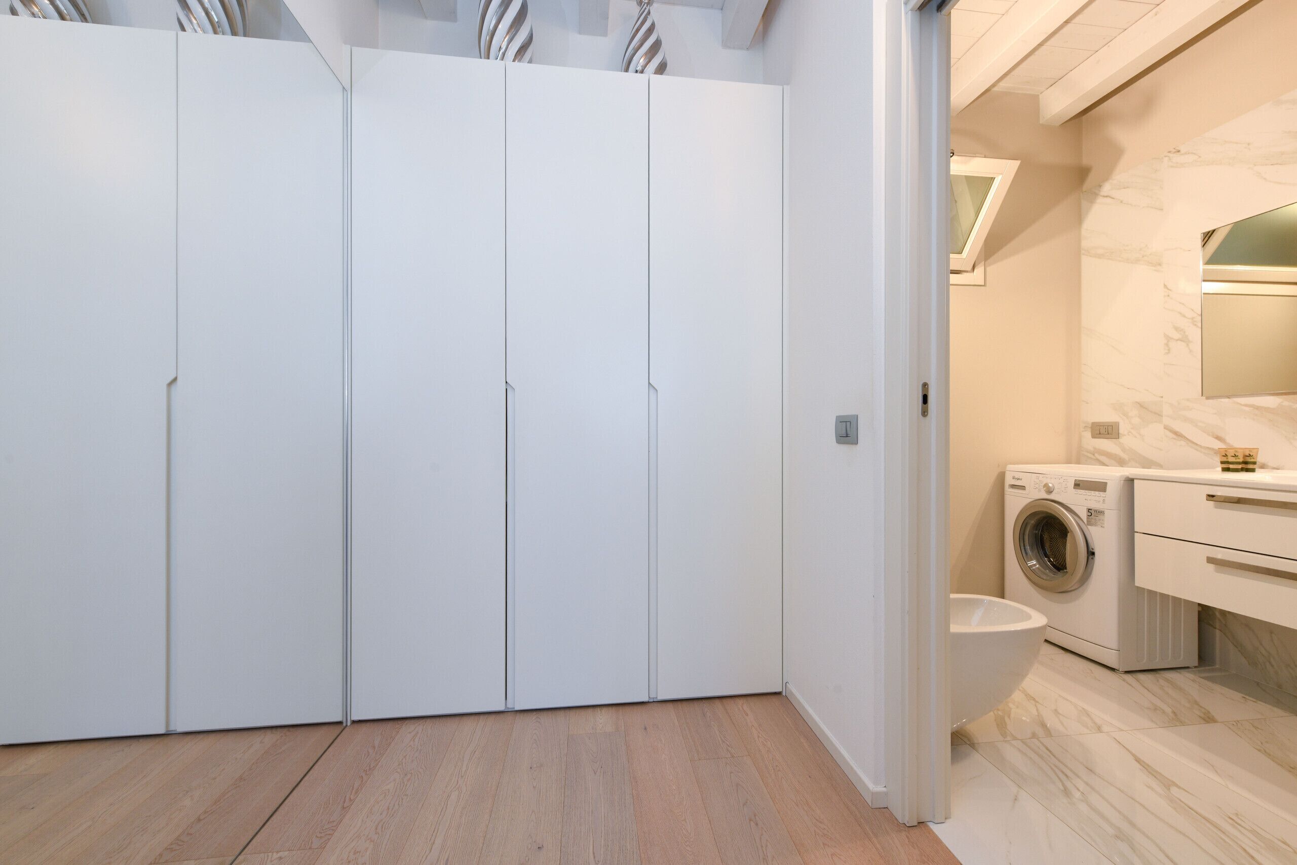 A modern bathroom with a built-in washing machine, a toilet, and a large mirror.