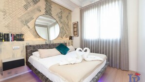 Ein Hotelzimmer mit einem großen Bett, einem runden Spiegel, einem Bücherregal mit Büchern und einem Fenster mit Vorhängen.