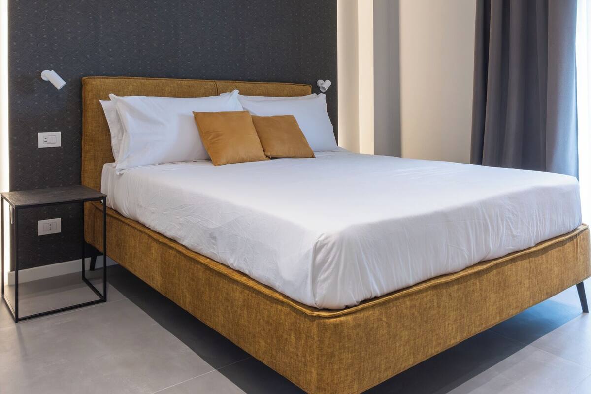 Una camera d'albergo moderna con un letto grande, un comodino e una parete scura.