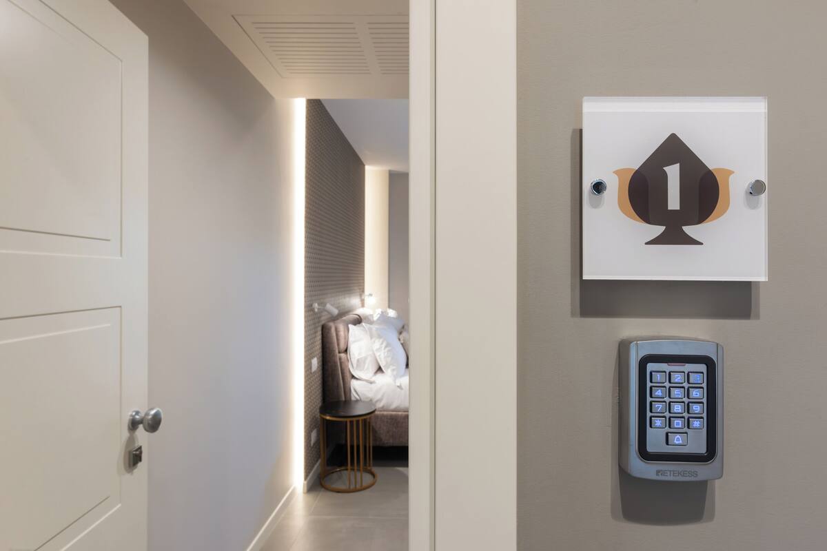 Una camera d'albergo con un letto, un comodino e un pannello di controllo a parete.