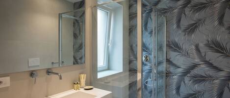 A modern bathroom with a glass-enclosed shower, a large mirror, and a window providing natural light.