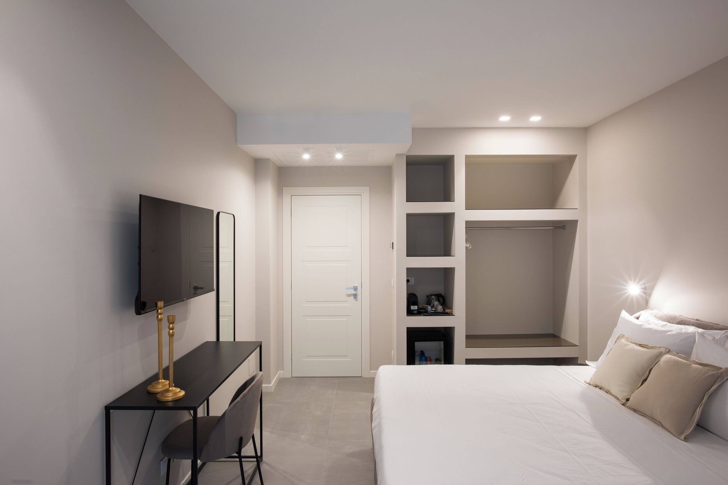 A modern bedroom with a bed, a desk with a TV, and a walk-in closet.