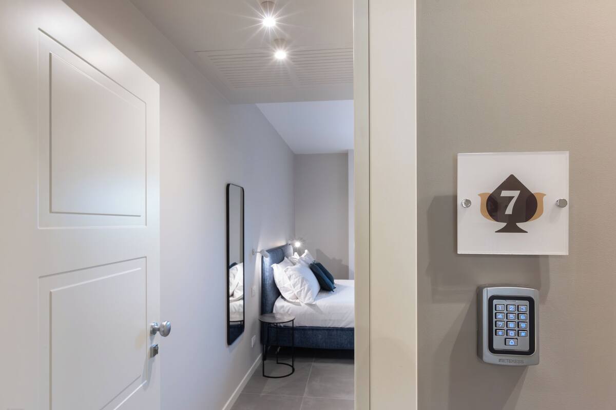 Una camera d'albergo con un letto, un comodino, uno specchio, un telefono fissato alla parete e una porta.
