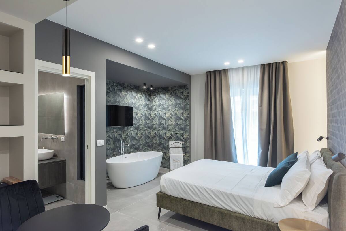Camera moderna con un letto grande, una vasca da bagno incassata e un bagno separato con una toeletta.