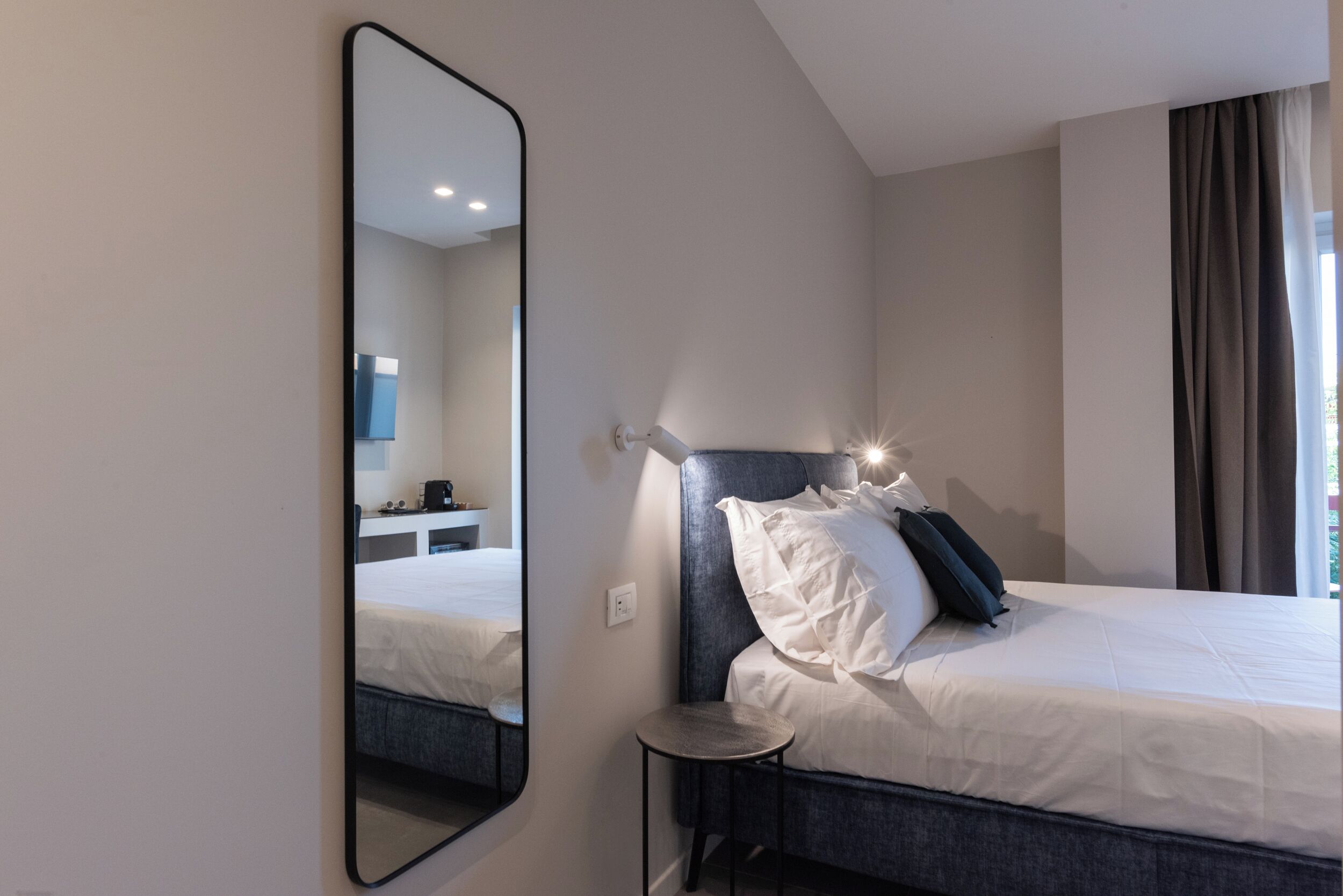 Habitación de hotel moderna con una cama grande, una mesita de noche, un espejo y vistas al baño.