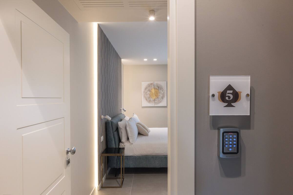 Camera d'albergo con un letto, un comodino, un pannello di controllo a parete e una porta.