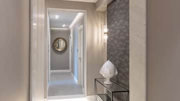 Un couloir moderne avec un sol en marbre, un miroir rond accroché au mur et une petite table sur laquelle est posé un objet décoratif.