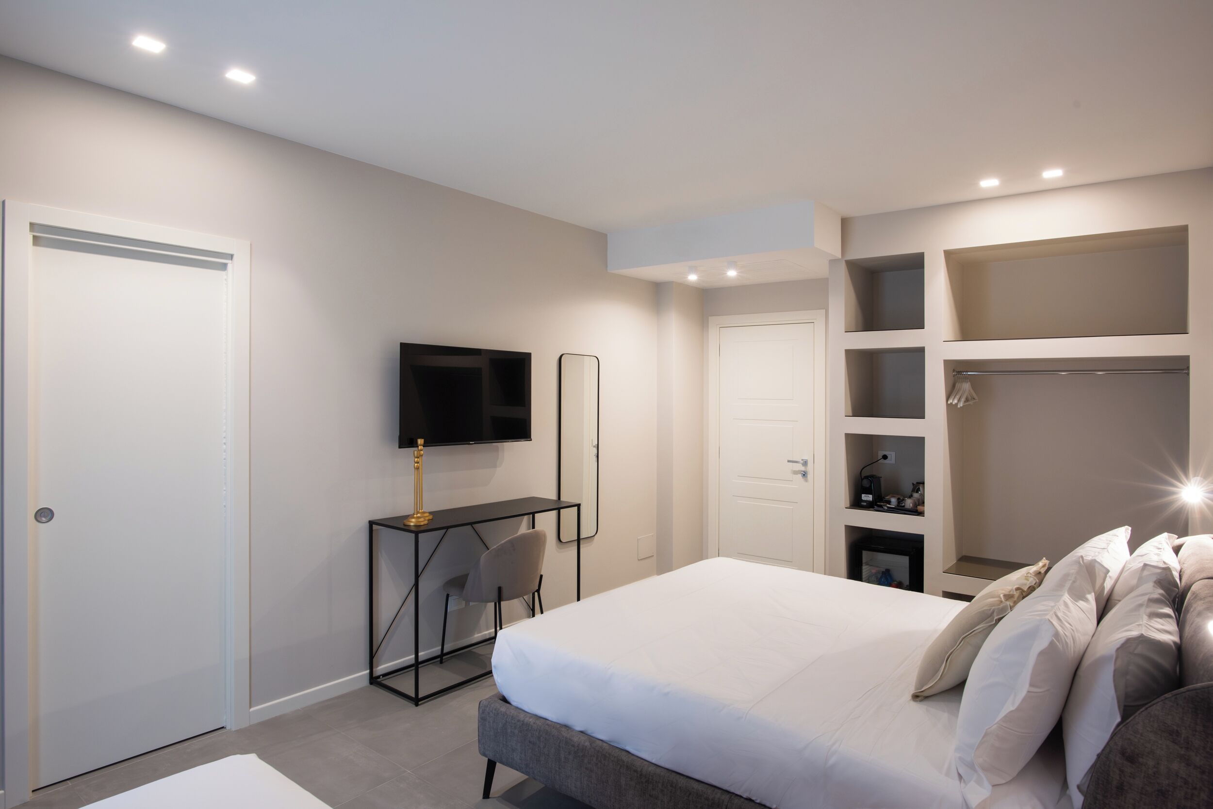 A modern bedroom with a bed, a desk, a TV, and built-in shelving.